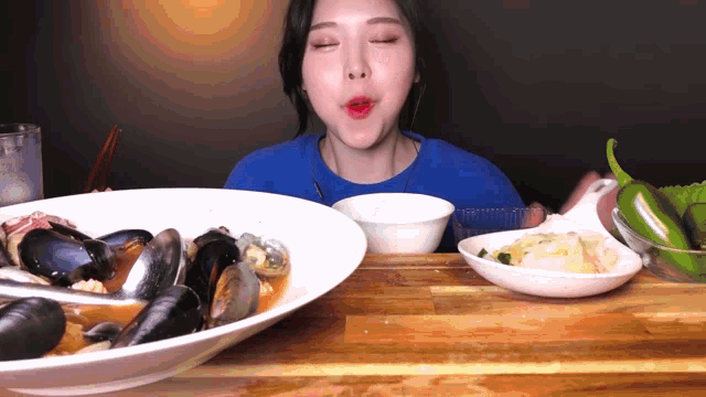 a woman in a blue shirt is eating a bowl of seafood