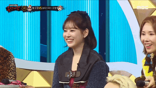 a woman is smiling while sitting in front of a mbc sign