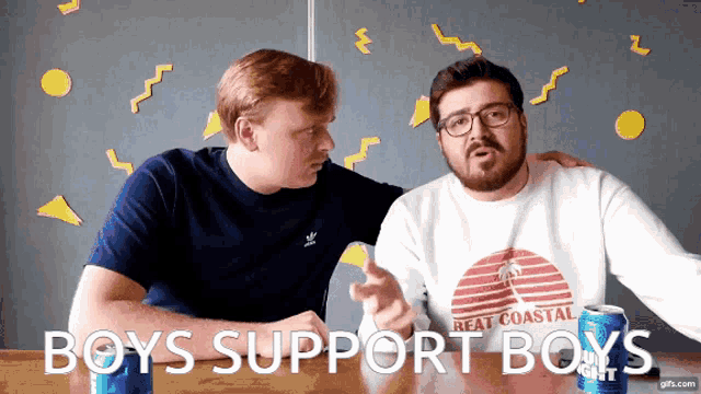 two men sitting at a table with the words " boys support boys " on the screen