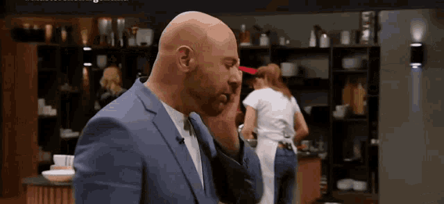 a bald man in a blue suit and tie is covering his face with his hand