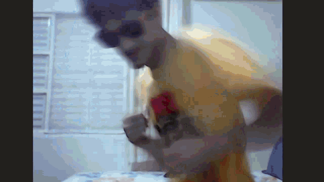 a man wearing sunglasses and a yellow shirt is dancing in front of a window