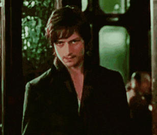 a man in a black jacket is standing in front of a window looking at the camera .