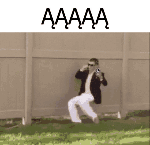 a man in a suit and white pants is standing in front of a fence while holding a can of soda .