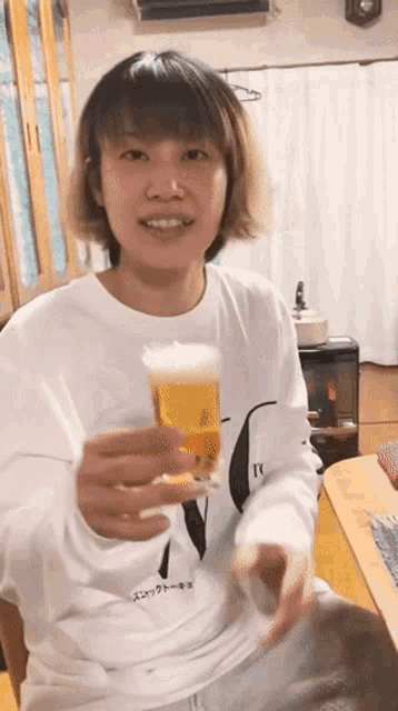 a woman in a white shirt is holding a glass of beer and smiling