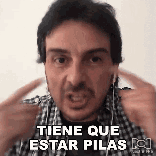 a man wearing ear buds and a plaid shirt says tiene que estar pilas