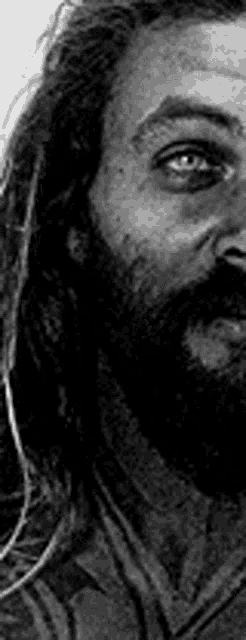 a man with dreadlocks and a beard is looking at the camera in a black and white photo .