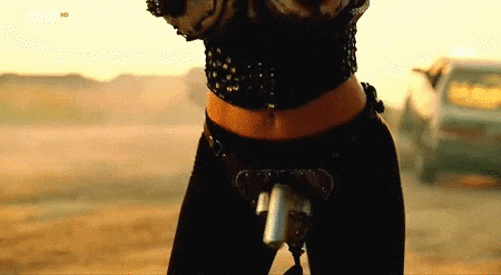 a woman in a black top and black pants is holding a gun in her hand .