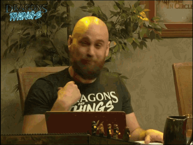 a man wearing a dragons and things shirt is sitting at a table