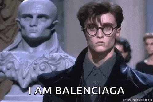 a man wearing glasses and a suit is standing in front of a statue and says i am balenciaga .