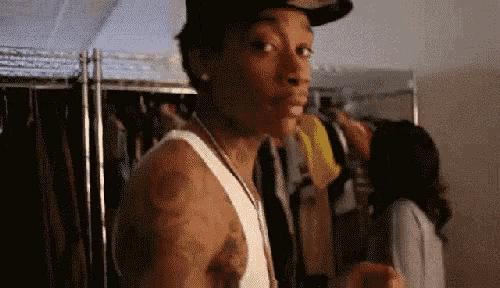 a man wearing a hat and a white tank top is standing in front of a closet .