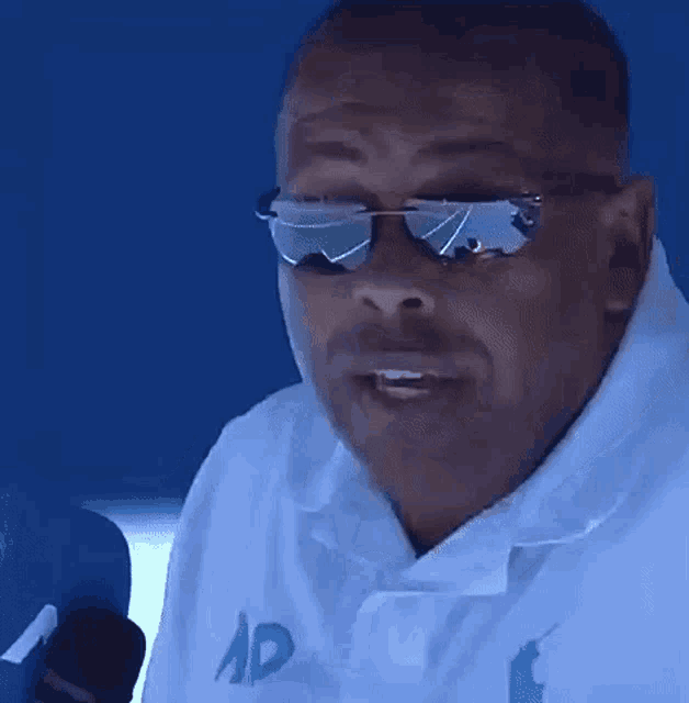 a man in a white shirt is making a funny face while sitting in front of a blue background .