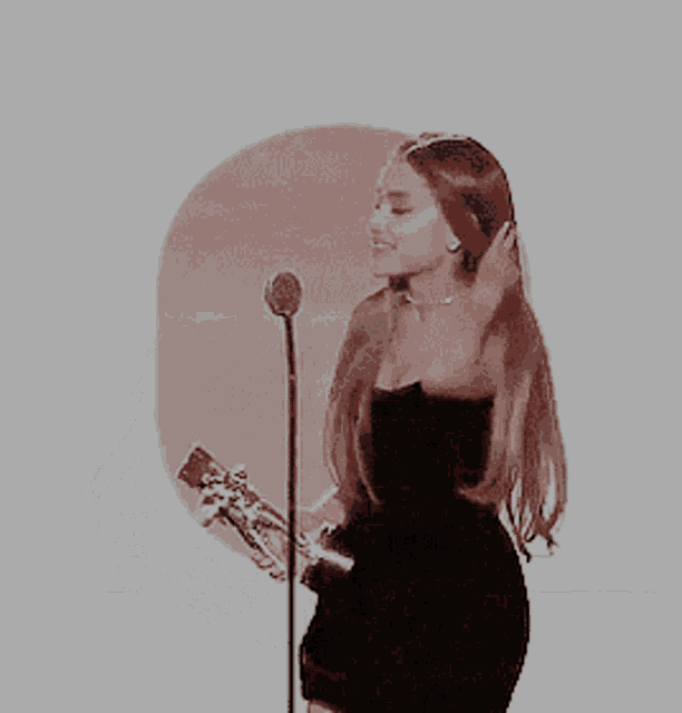 a woman in a black dress is holding a guitar and singing into a microphone