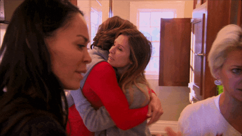 a woman in a red vest is hugging another woman in a kitchen