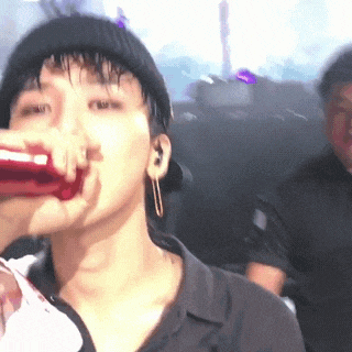 a man is drinking from a red bottle while wearing a hat and earrings .