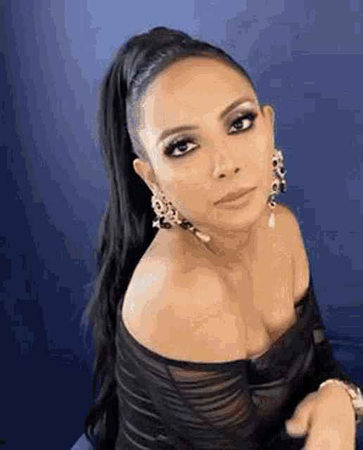 a woman wearing a black dress and earrings is sitting in front of a blue wall .