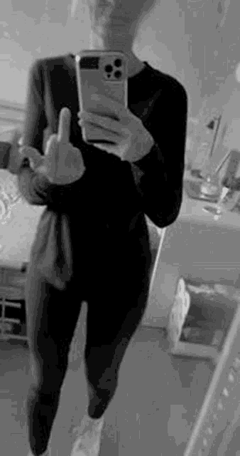 a woman is taking a selfie in front of a mirror while holding a cell phone and giving the middle finger .