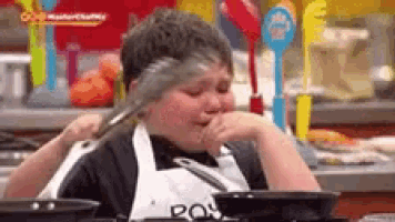a young boy in an apron is holding a spatula over his face .