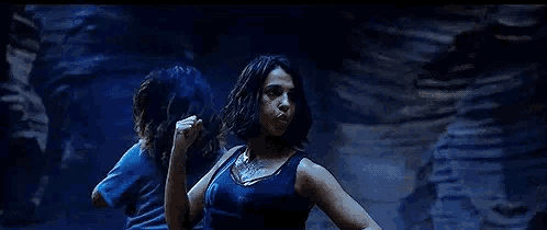 a woman in a blue tank top is dancing in front of a rock wall .