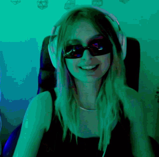 a woman wearing sunglasses and headphones smiles in a dark room