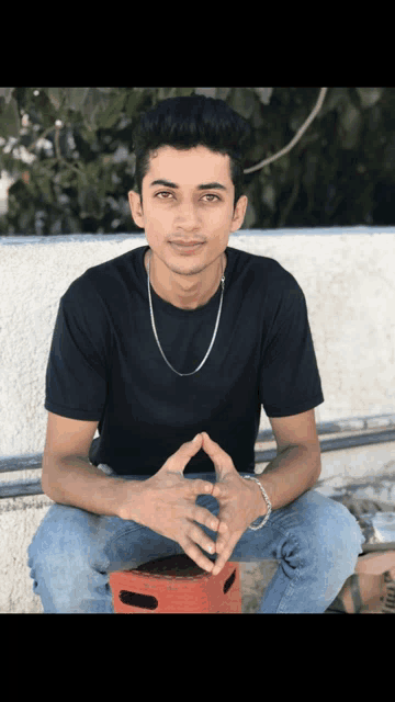 a young man wearing a black t-shirt sits on a red stool
