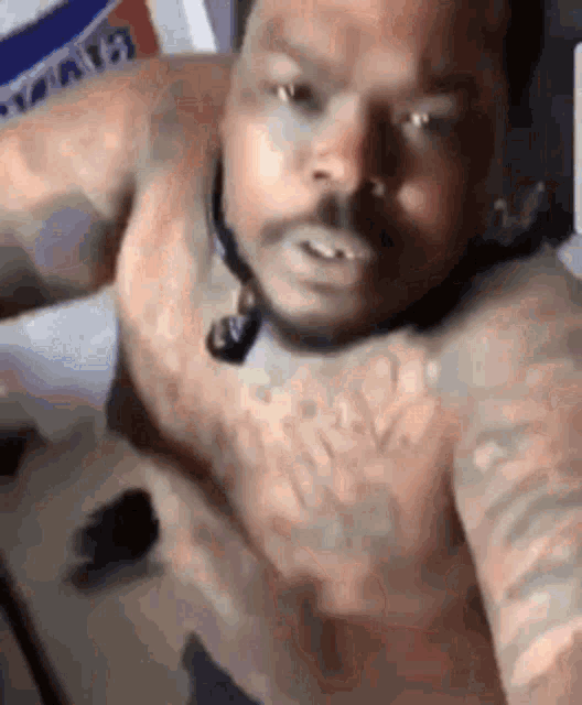 a shirtless man with tattoos on his chest is taking a selfie with his phone .