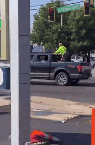 a man in a neon green shirt sits in the back of a truck under a sign that says lingberg dr.