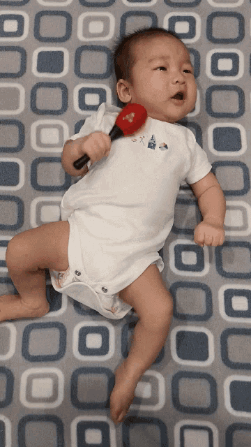 a baby is laying on a blanket holding a red maracas