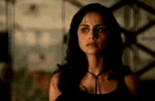 a woman in a black tank top is standing in a dark room and looking at the camera .