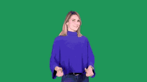 a woman in a blue sweater is standing in front of a green screen and making a funny face .