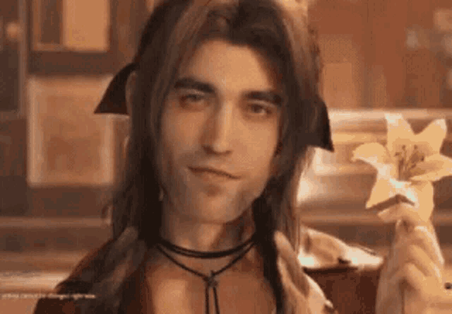 a man with long hair and a choker is holding a flower in his hand .