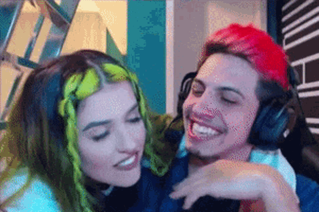 a man with red hair is hugging a woman with green hair while wearing headphones .