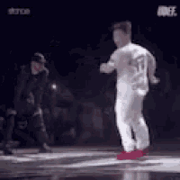 a man in a white shirt is dancing on a stage while a referee watches .