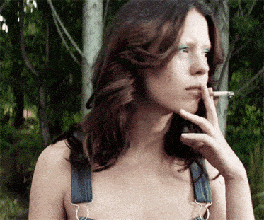 a woman in overalls smoking a cigarette outdoors