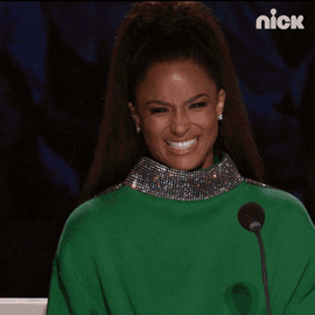 a woman in a green sweater is smiling in front of a microphone with the nick logo on the bottom