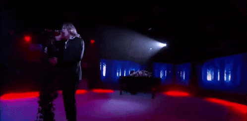 a man in a suit is holding a camera in a dark room with purple lights .