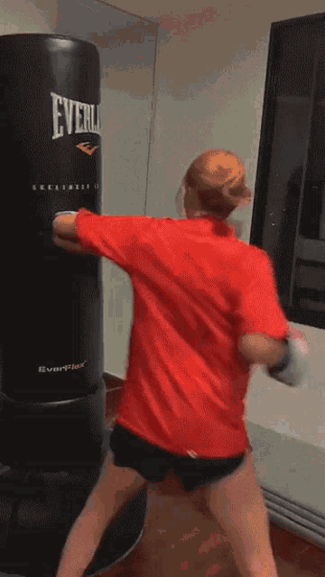 a woman wearing boxing gloves is standing in front of a everlast heavy bag