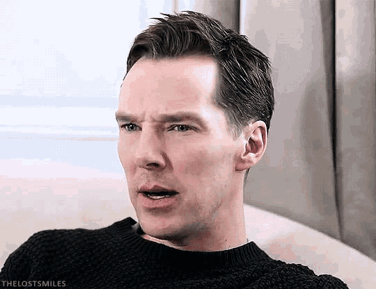 a man wearing a black sweater is sitting on a couch making a funny face .