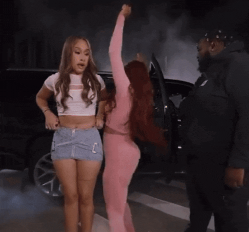 two women are standing next to each other in front of a black car