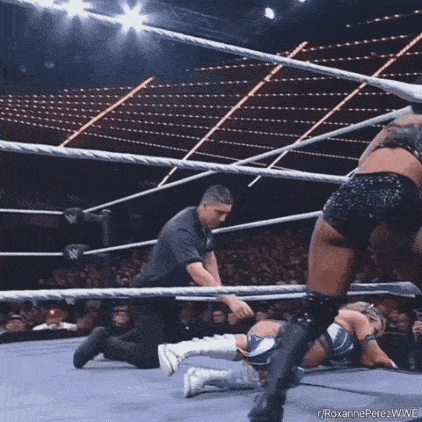 a referee is kneeling down in a wrestling ring while a wrestler is laying on the ground .