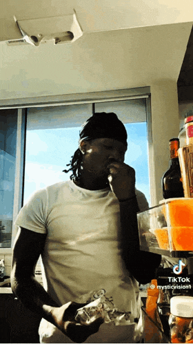 a man smoking a cigarette in a kitchen with a bottle of ketchup on the shelf behind him
