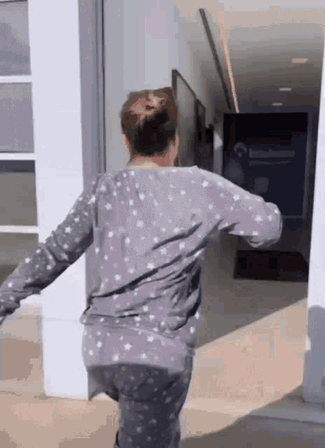 a woman wearing a gray pajama set is standing in a hallway