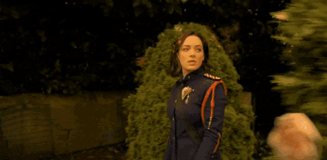 a woman in a military uniform stands in front of a bush with flowers