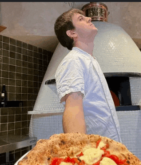 a man standing in front of a large pizza oven