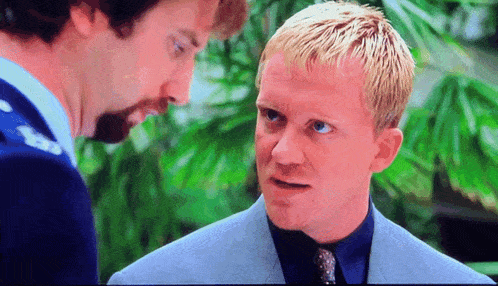 a man with blonde hair and blue eyes talks to another man