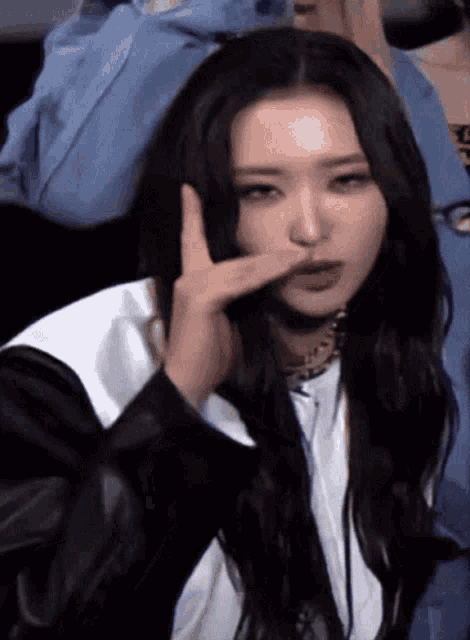 a woman with long black hair is making a funny face with her finger in her nose .