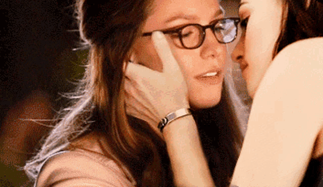 two women wearing glasses are kissing each other .