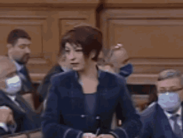 a woman with short hair is standing in front of a crowd of people wearing masks .