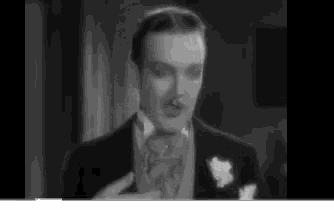 a man in a tuxedo is holding a glass of wine in a black and white photo .