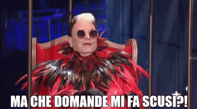 a man in a red feathered costume is sitting in a chair with sunglasses on .