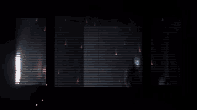 a dark room with blinds on the windows and a light shining through them